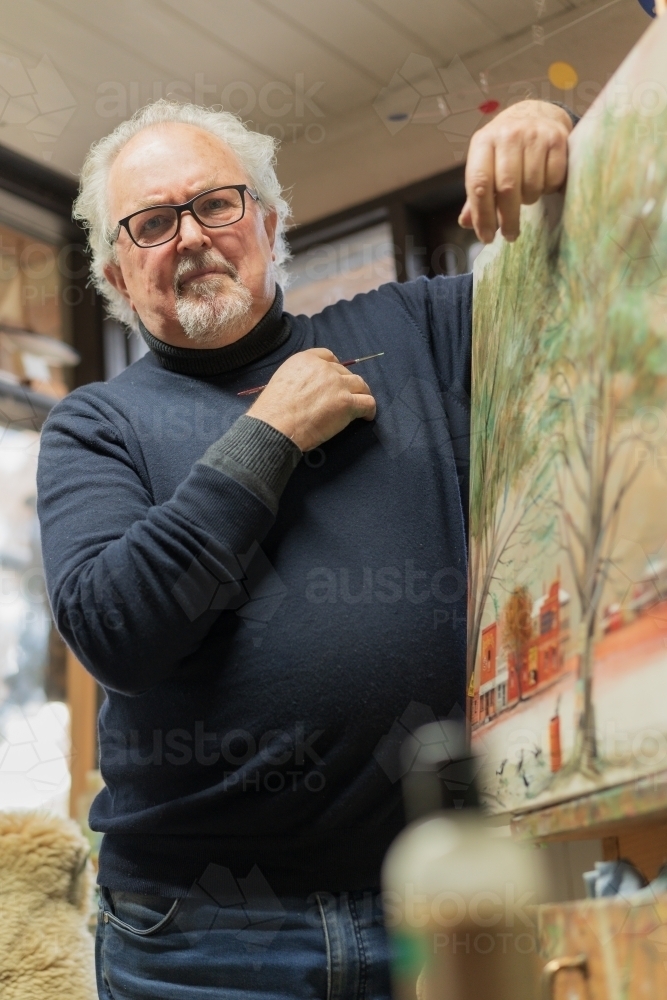 Low angled view of a distinguished male artist leaning on a painting in an art studio - Australian Stock Image
