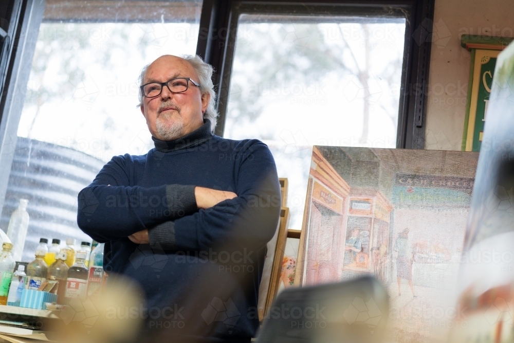 Low angled view of a distinguished male artist standing with folded arms in an art studio - Australian Stock Image