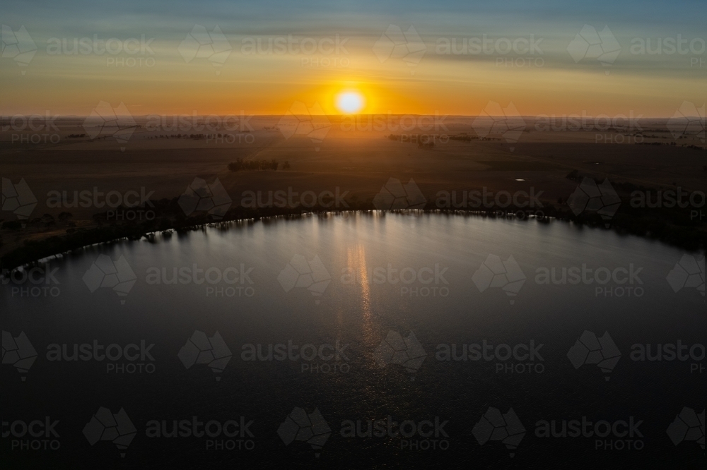 Low sun over landscape with lake in foreground - Australian Stock Image