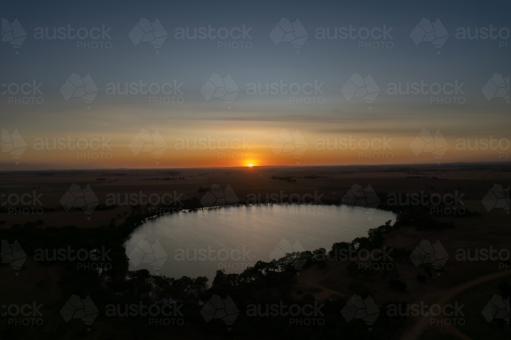 Low sun over landscape with lake in foreground - Australian Stock Image