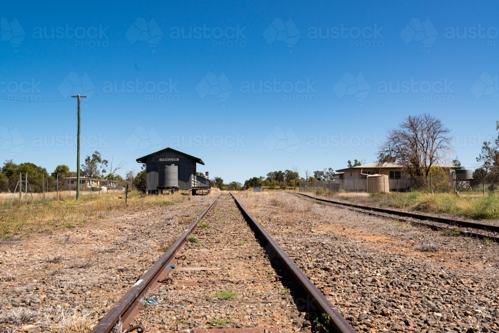 Low view along railway lines to a country station with a blue sky - Australian Stock Image