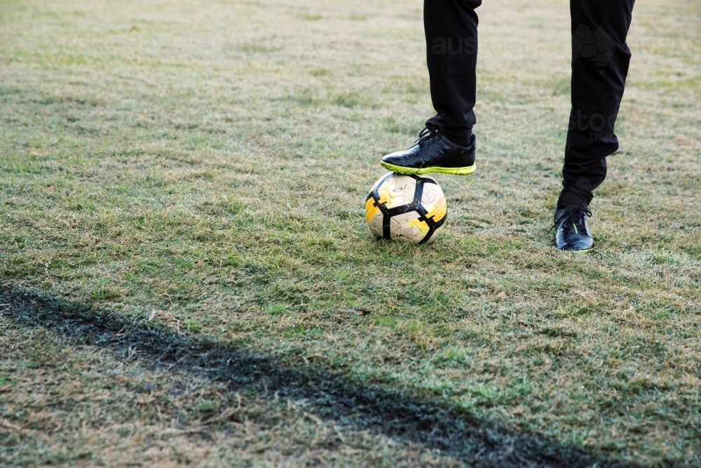 Lower body extremity shot of a man standing on the field stepping on a soccer ball with one foot - Australian Stock Image