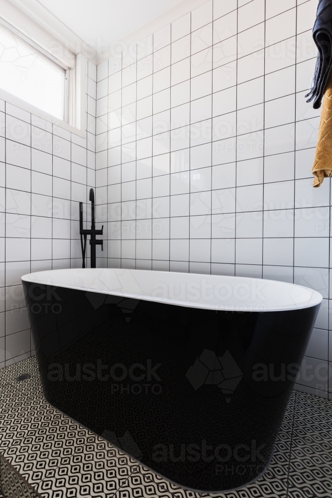 Image of Luxury stand alone black bathtub in a dully tiled bathroom