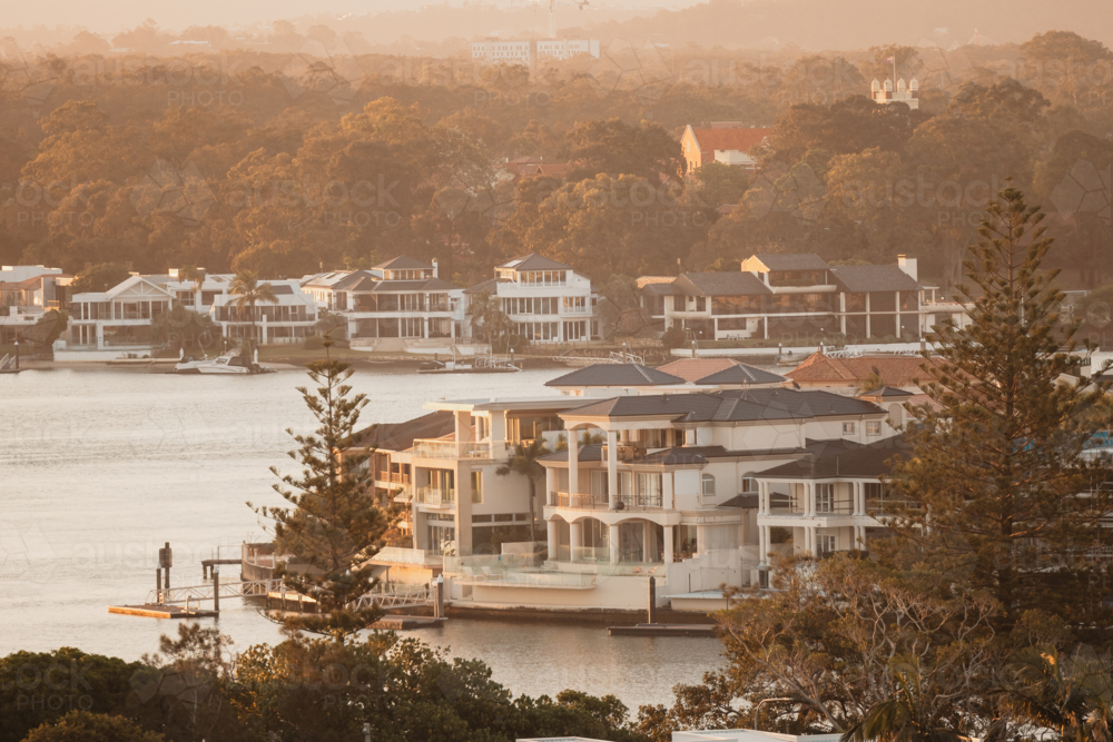 Luxury waterfront mansions line a serene river at golden hour - Australian Stock Image