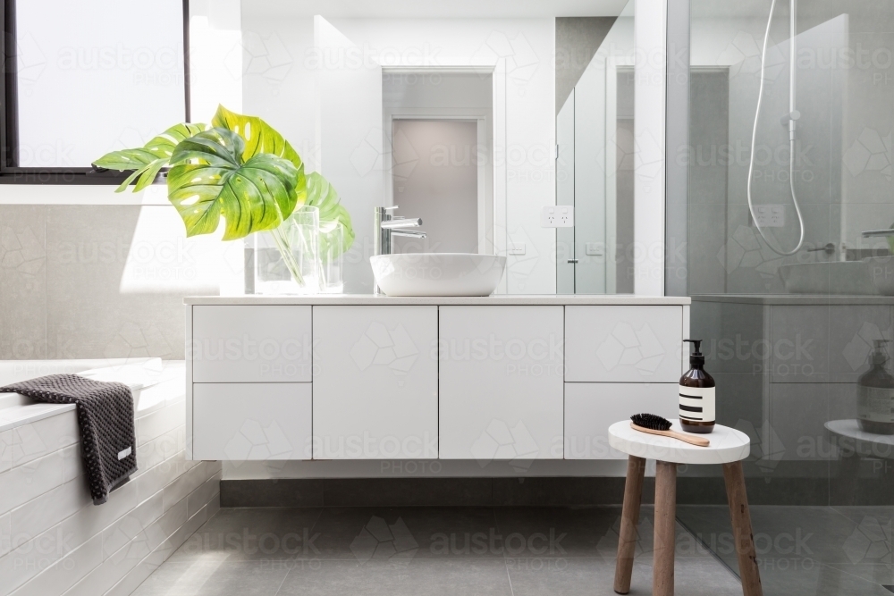 Luxury white family bathroom styled with greenery and a wooden stool - Australian Stock Image