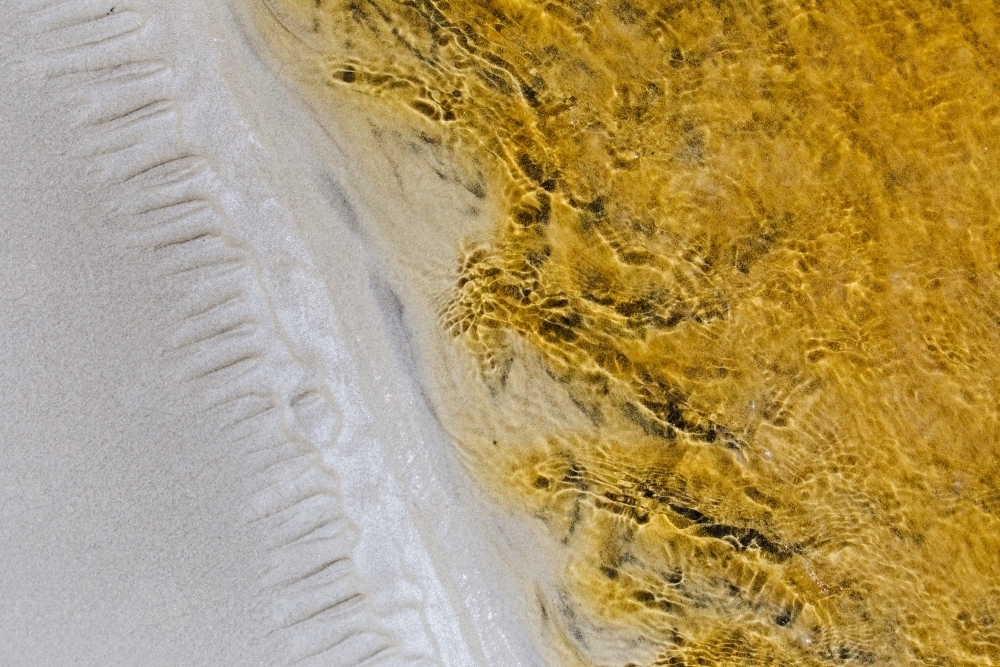 Macro close-up of patterns in the sand and stream with tannins in the water - Australian Stock Image