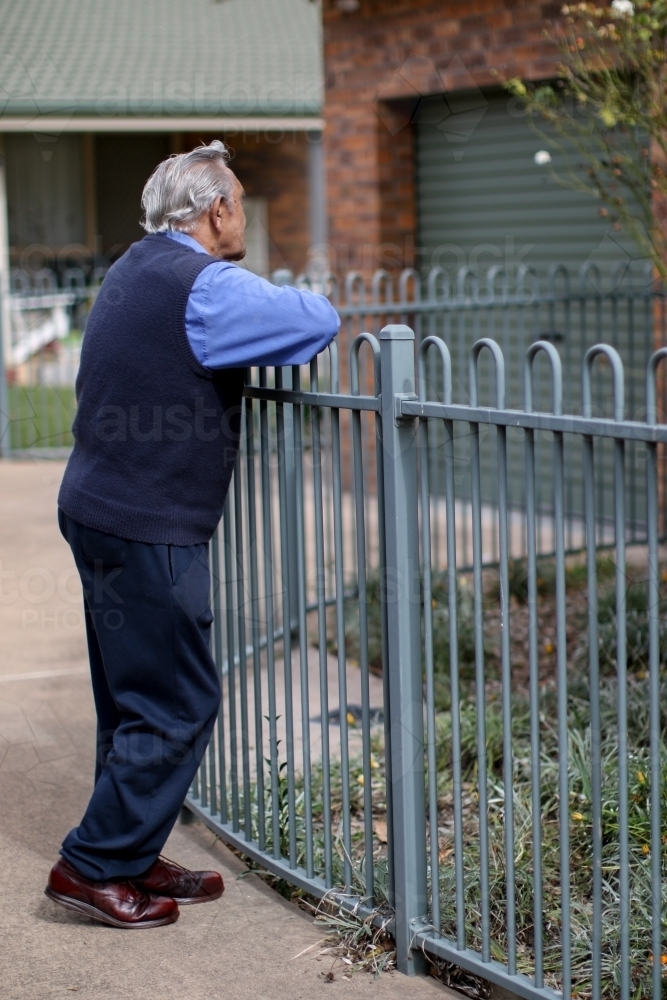 Male Aboriginal elder leaning against a fence turned away from the camera - Australian Stock Image