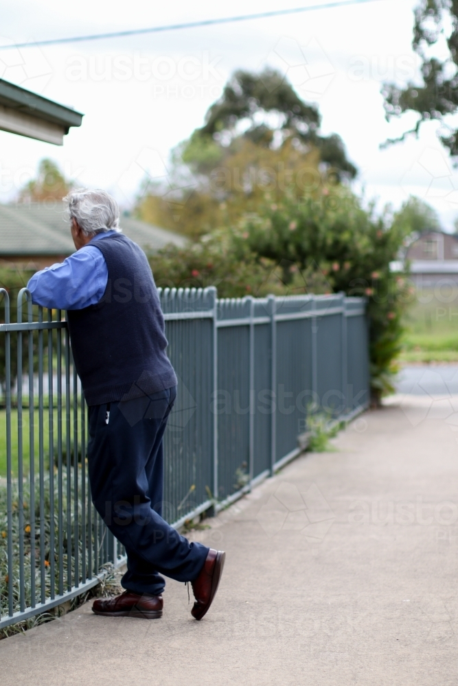 Male Aboriginal elder leaning against a metal fence - Australian Stock Image