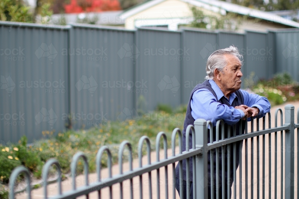 Male Aboriginal elder leaning against fence looking away - Australian Stock Image