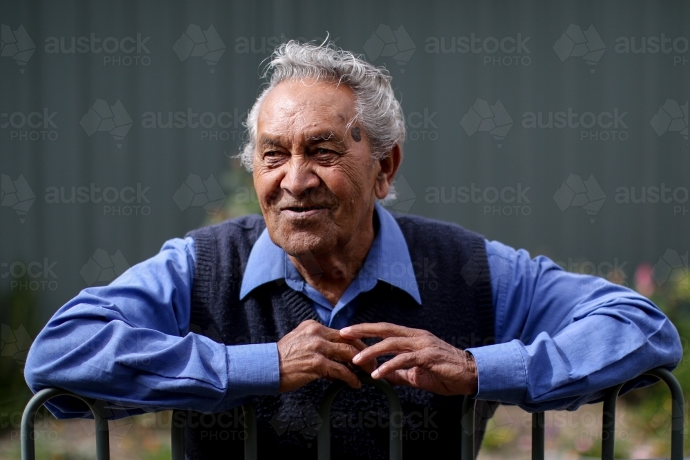 Male Aboriginal elder smiling and leaning against fence - Australian Stock Image