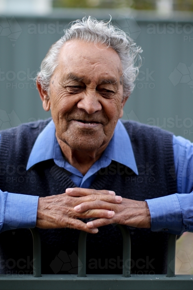Male Aboriginal elder smiling and leaning against fence - Australian Stock Image