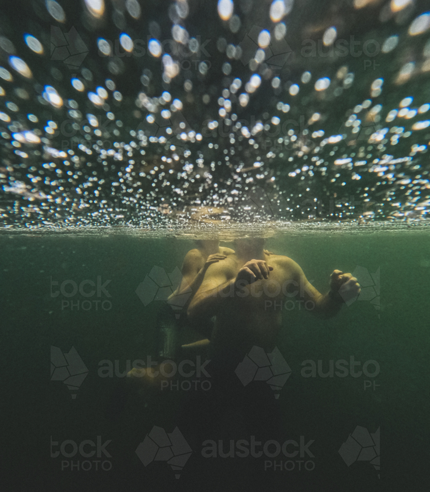 Male adult with child on back underwater with bubbles on water surface - Australian Stock Image