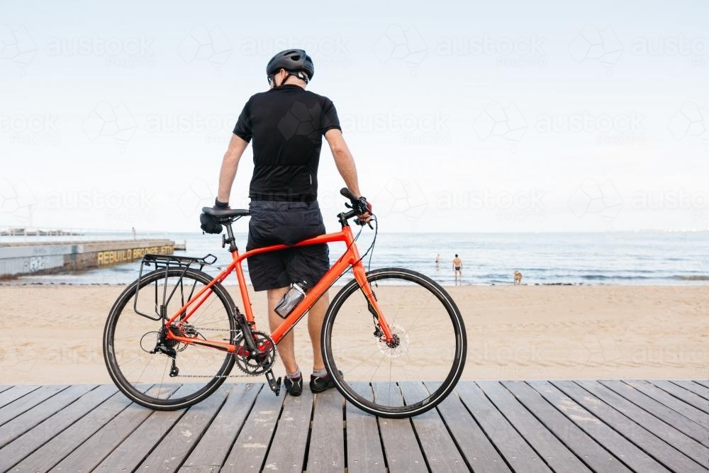 Male bike rider leaning against bike viewing the beach - Australian Stock Image