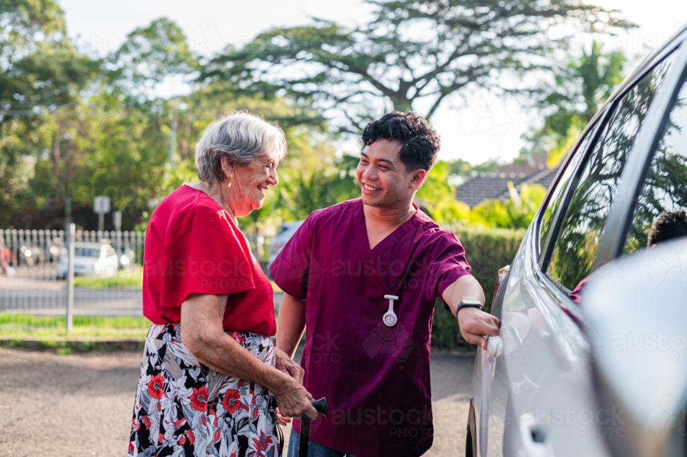 Male caregiver helping an elderly woman get into the vehicle - Australian Stock Image