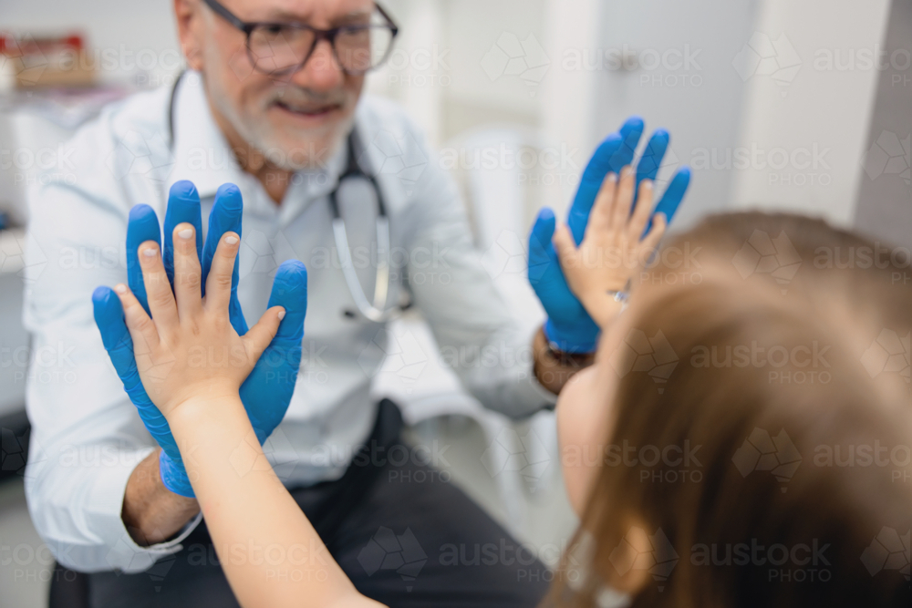 Male doctor doing high five with young girl inside exam room - Australian Stock Image