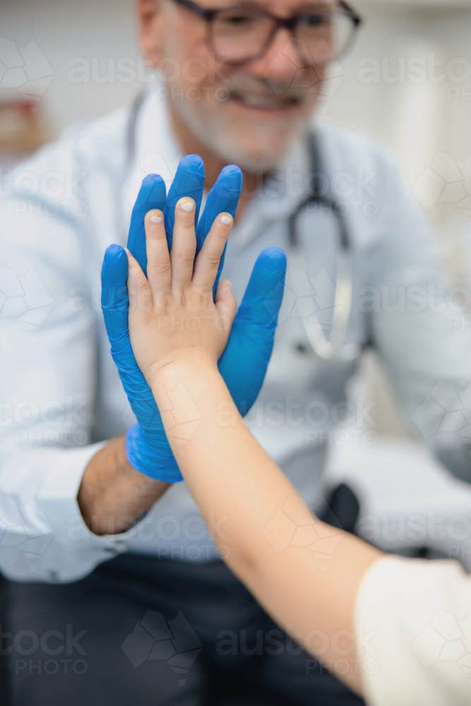 Male doctor doing high five with young girl inside exam room - Australian Stock Image