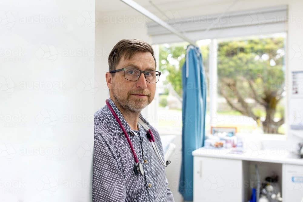 Male doctor with a stethoscope around his neck leaning on the wall - Australian Stock Image