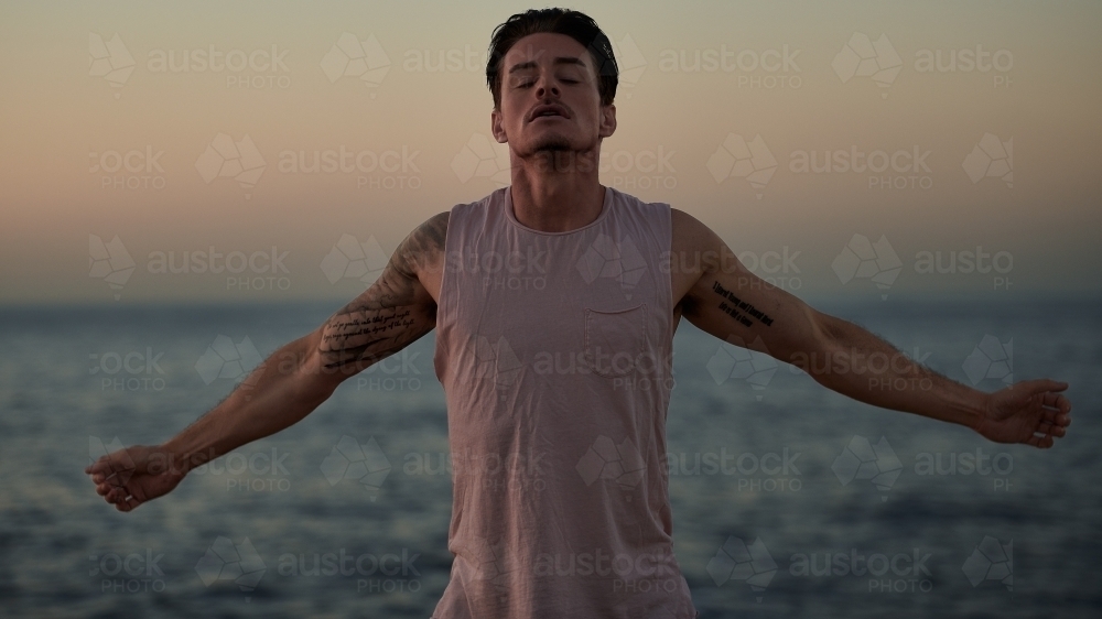 Male doing stretch exercise beside ocean - Australian Stock Image