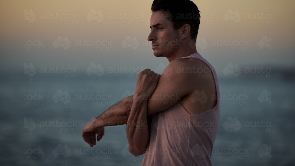Male doing stretch exercise beside ocean - Australian Stock Image
