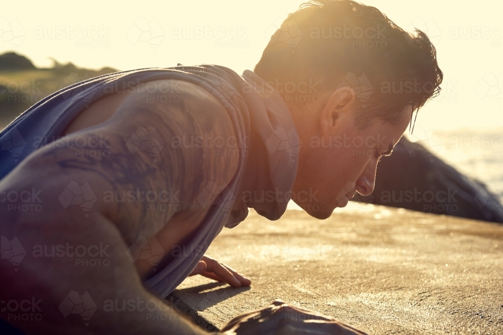 Male doing stretch exercise beside ocean - Australian Stock Image