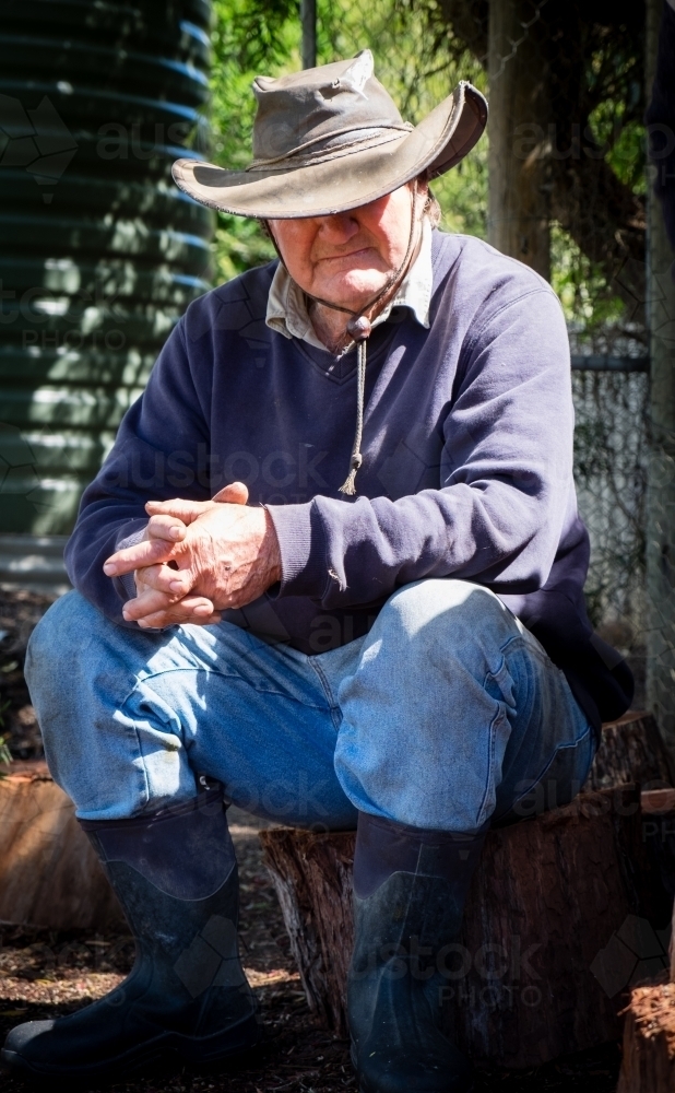 Male Farmer Sitting on the wood pile taking a break - Australian Stock Image