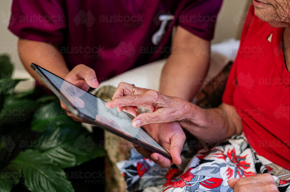 Male healthcare worker holding tablet device for an elderly woman tapping on the screen - Australian Stock Image