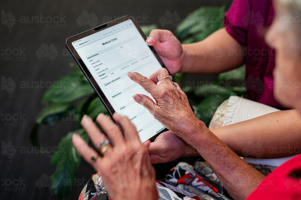Male healthcare worker holding tablet device for an elderly woman tapping on the screen - Australian Stock Image
