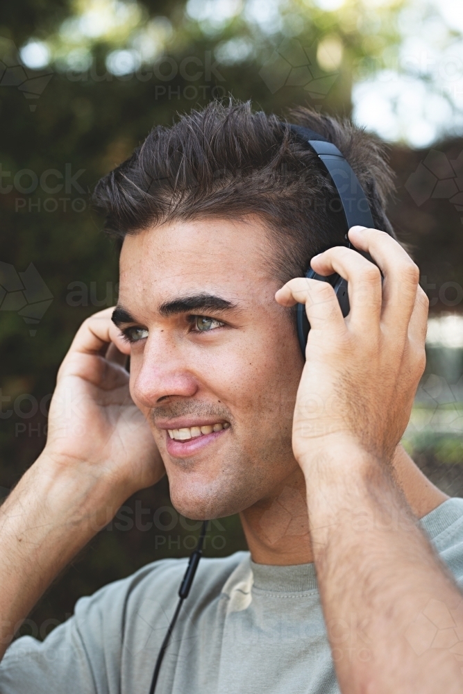 Male in his twenties wearing headphones and listening to music outdoors in the local park - Australian Stock Image