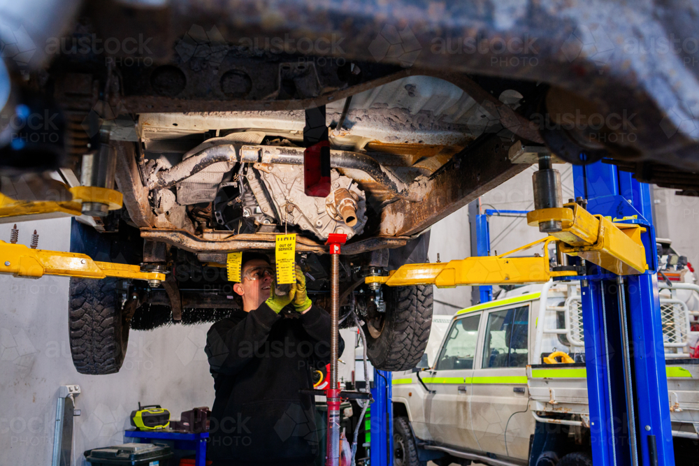 Image of Male mechanic working under vehicle raised on a hydraulic lift ...