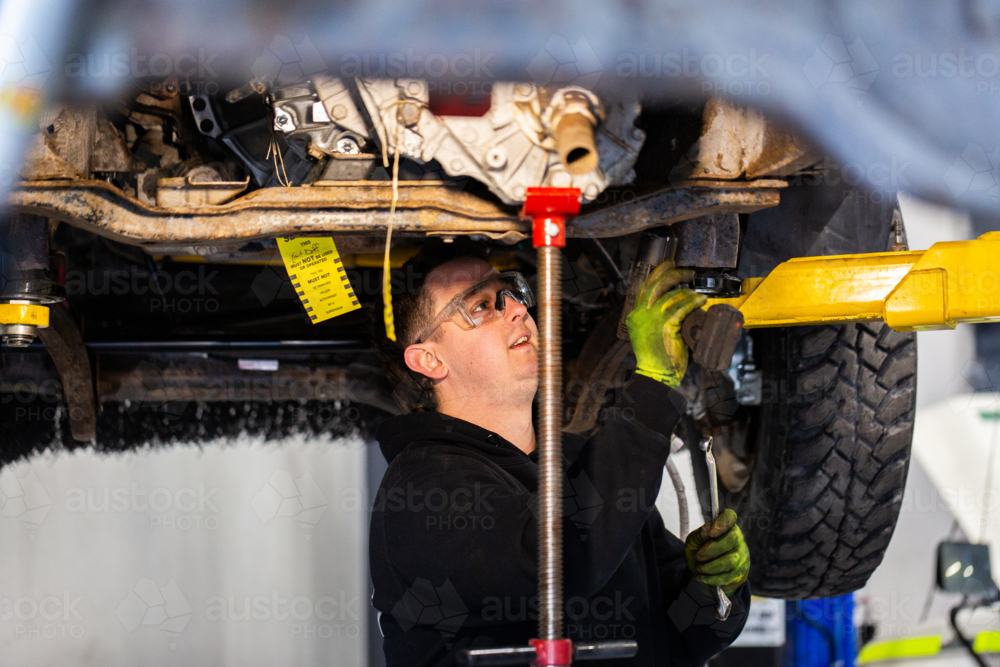 Image of Male mechanic working under vehicle raised on a hydraulic lift ...