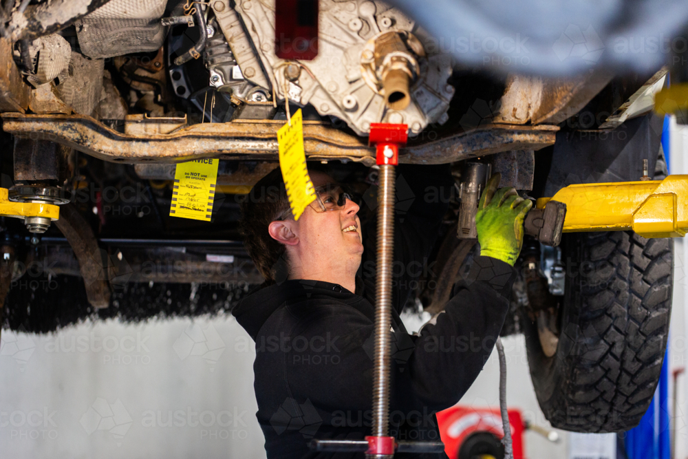 Image of Male mechanic working under vehicle raised on a hydraulic lift ...