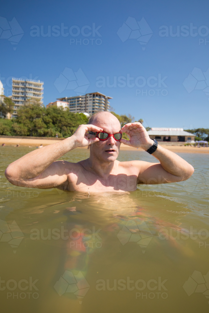 Male middle aged swimmer adjusting goggles while standing in the water - Australian Stock Image