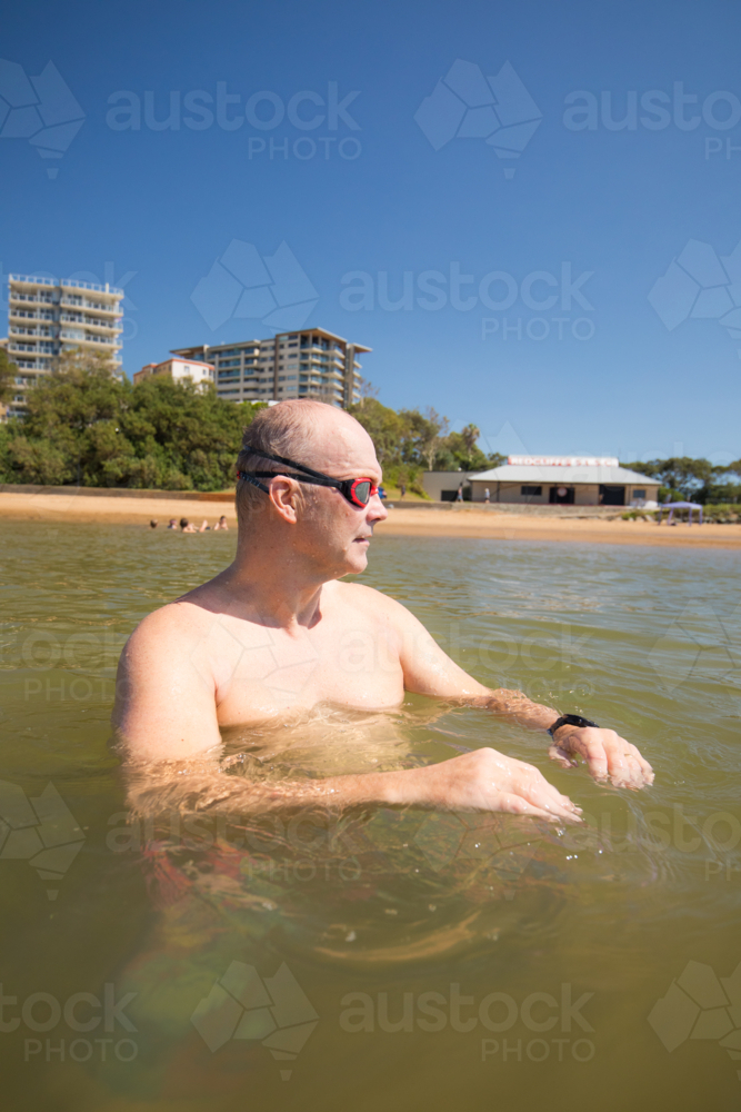 Male open water swimmer wearing goggle standing in water near the shore - Australian Stock Image