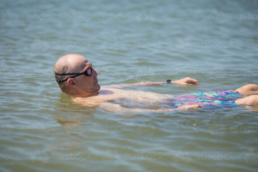Male open water swimmer wearing goggles float on back in water - Australian Stock Image
