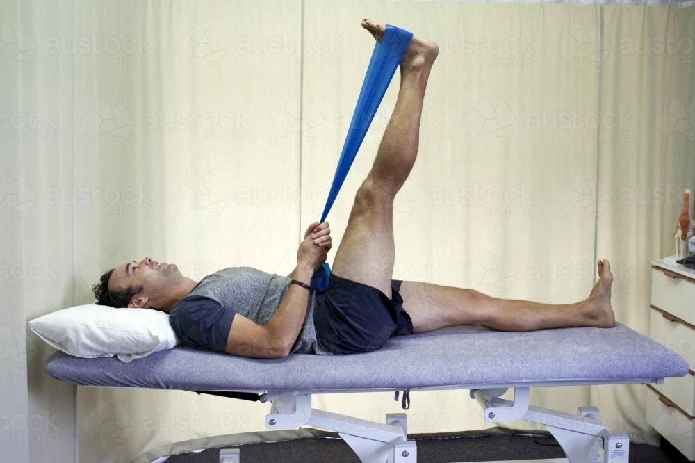 Male patient completing a hamstring stretch on a bed in a physio studio - Australian Stock Image