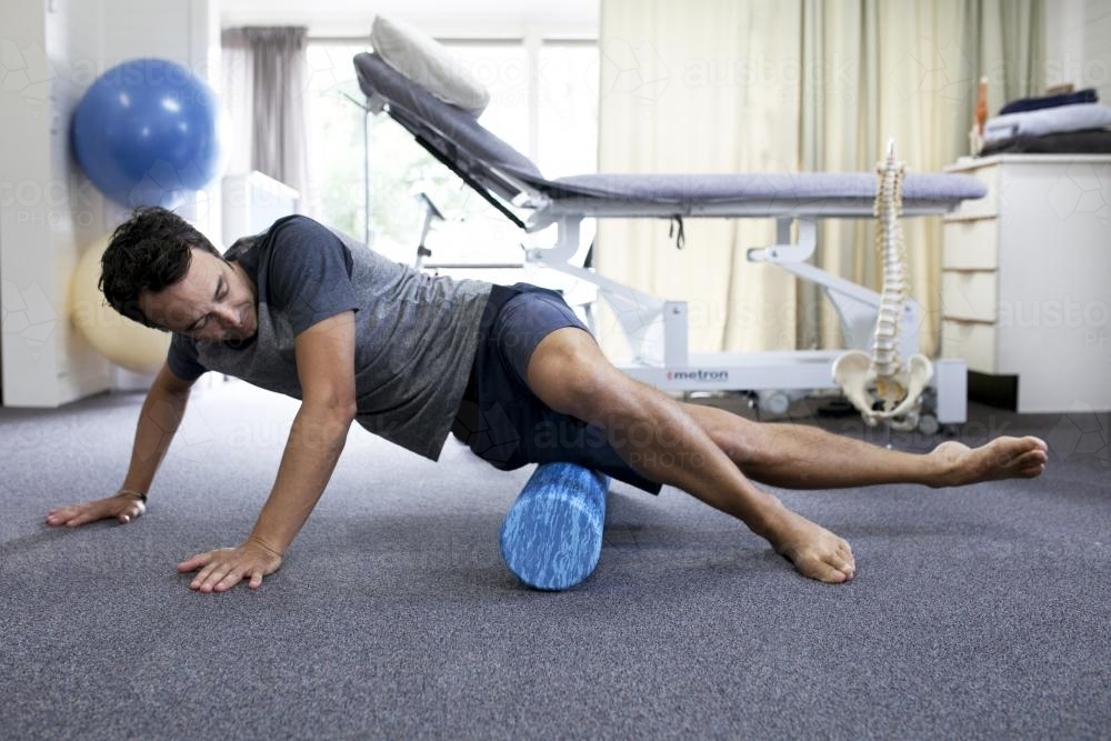 Male patient using a foam roller in a physio studio - Australian Stock Image