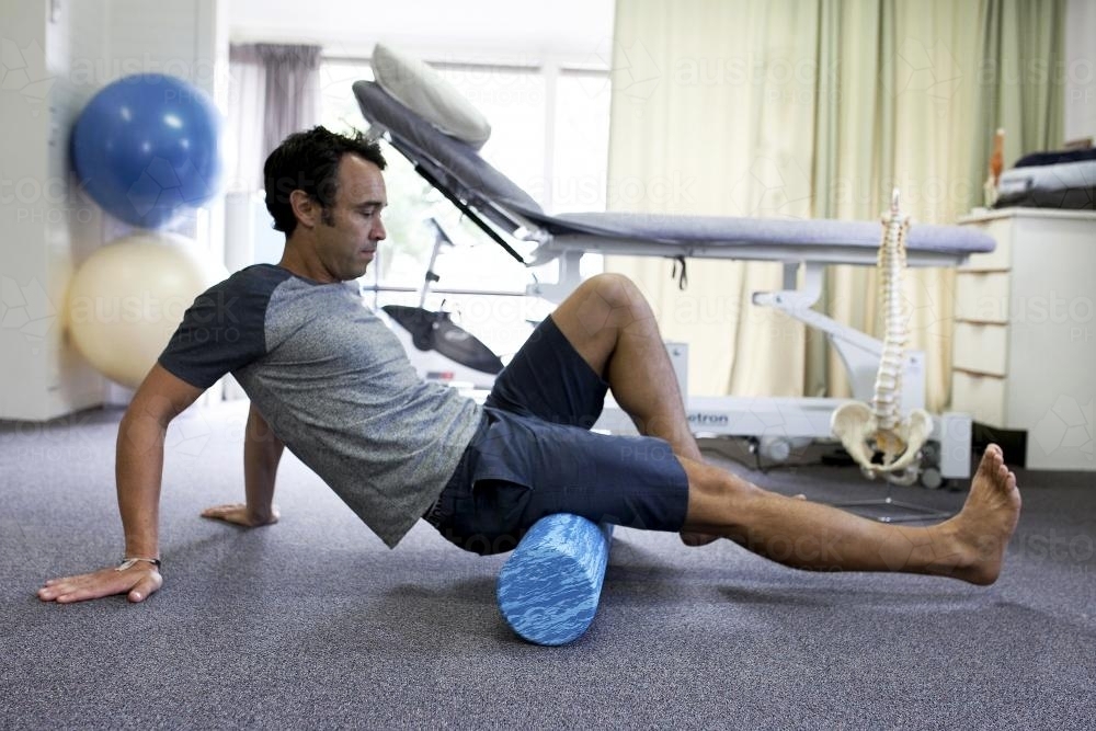 Male patient using a foam roller in a physio studio - Australian Stock Image
