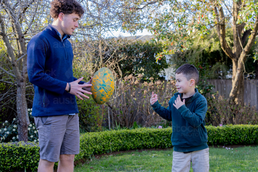 Male siblings passing the footy to each other in the backyard - Australian Stock Image