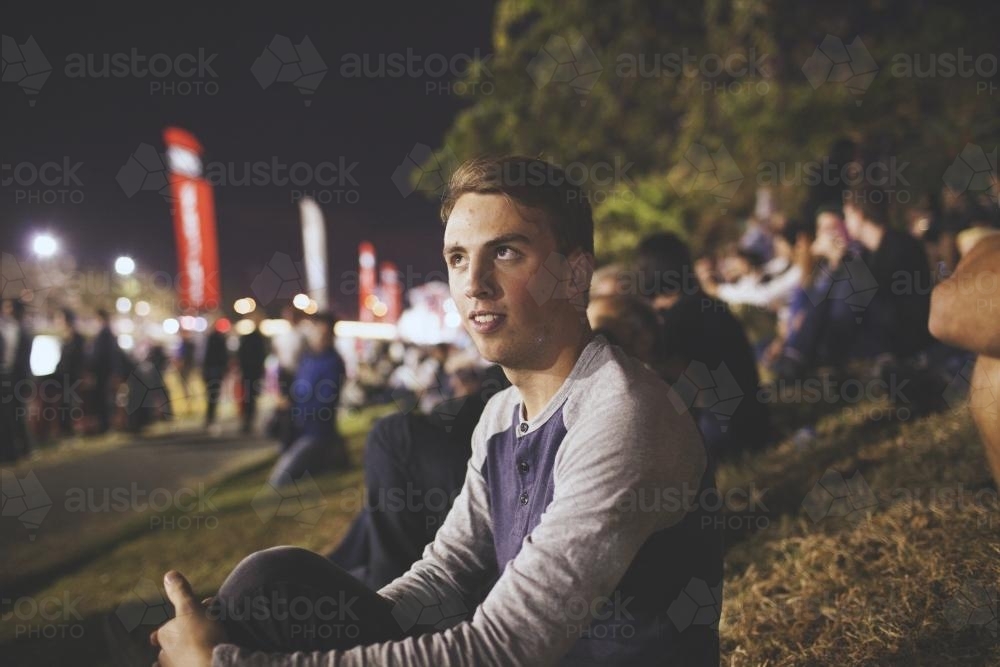 Image of Male spectator sitting on grass at an event - Austockphoto