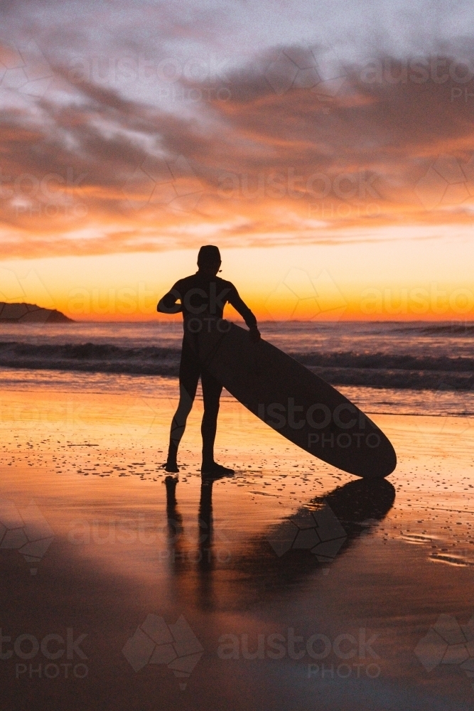 Male surfer getting ready to paddle out at sunrise - Australian Stock Image