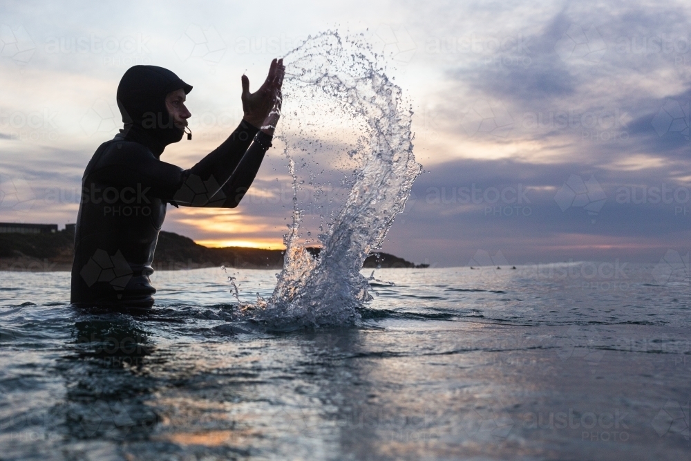 Male surfer splashing in water during sunrise - Australian Stock Image