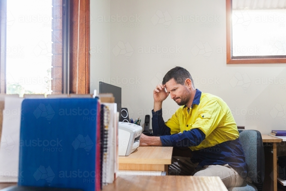 Male tradie at home office desk feeling overwhelmed and exhausted - Australian Stock Image