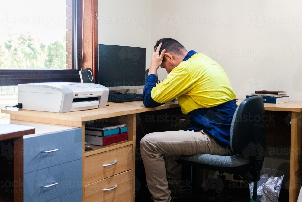 Male tradie at home office desk feeling overwhelmed and exhausted - Australian Stock Image