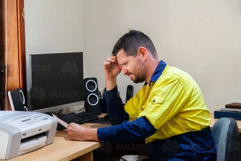 Male tradie in his 30's sitting at his computer stressed out over paperwork - Australian Stock Image