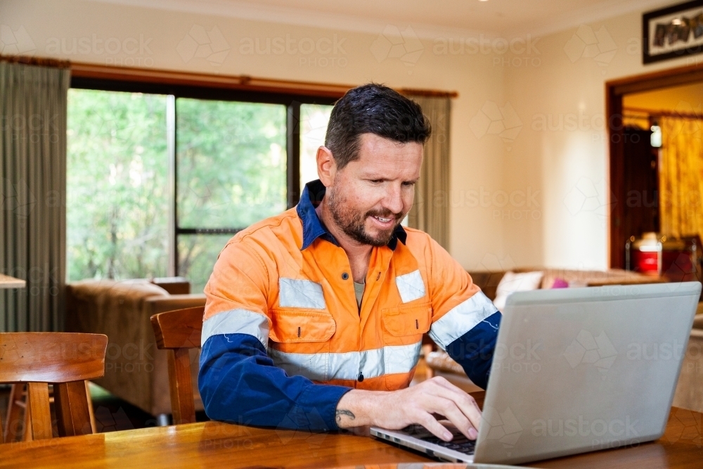 Male tradie in his 30s on laptop feeling overwhelmed and exhausted - Australian Stock Image