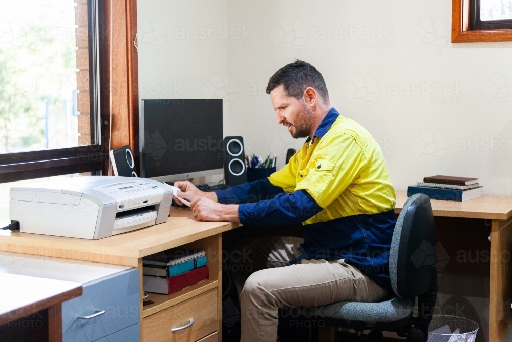 Male tradie looking at bills in home office - Australian Stock Image