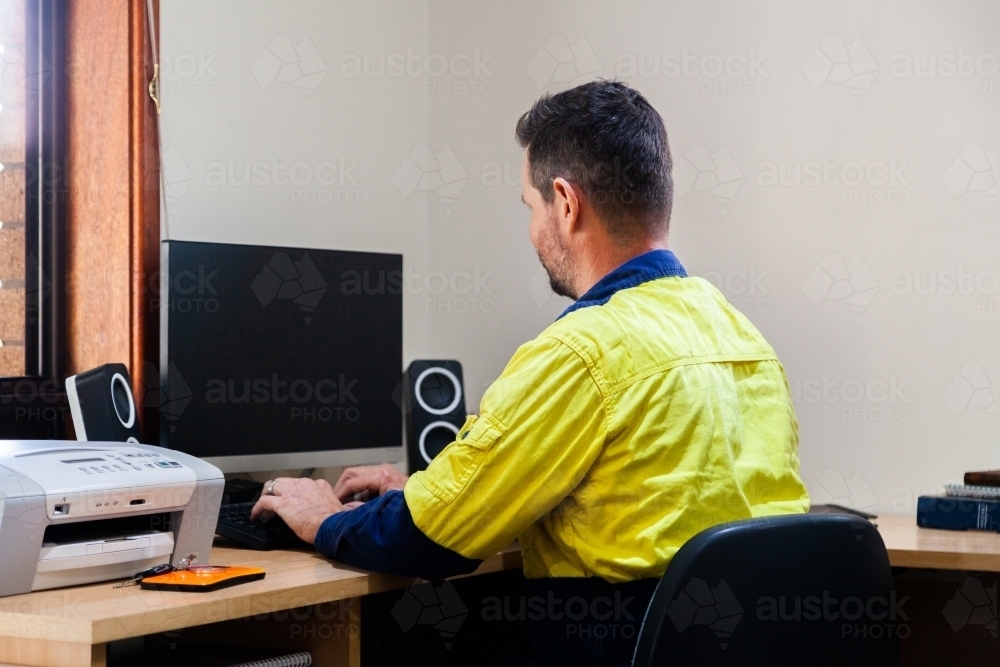 Male tradie using computer in home office - Australian Stock Image