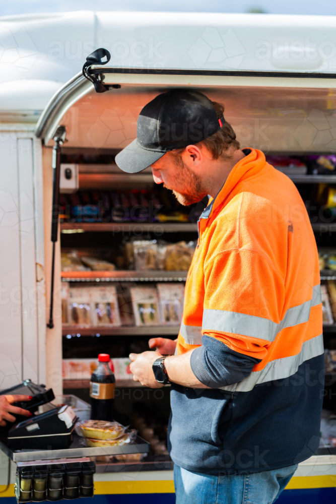 male worker on lunch break at industrial workplace purchasing snacks to eat - Australian Stock Image
