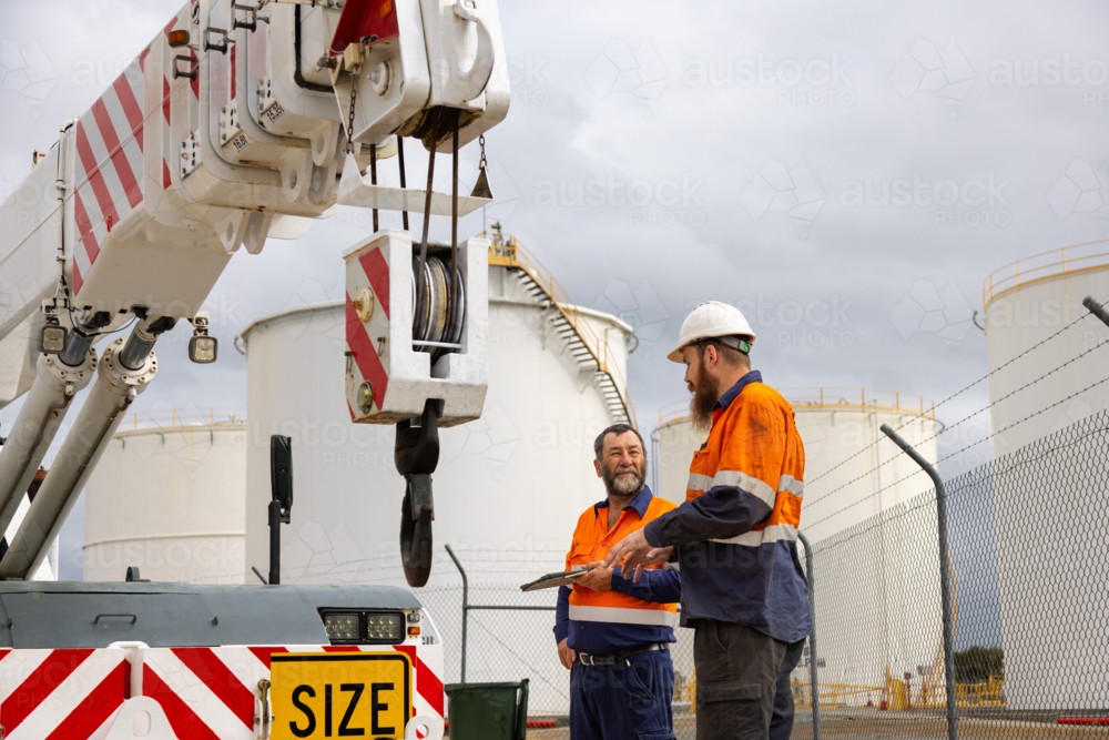 Male workers talking together by pick and carry franna crane on industrial site - Australian Stock Image