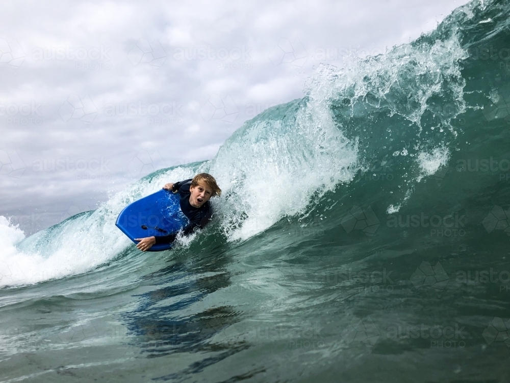 Image of Male youth surfing wave on boogie board in ocean Austockphoto